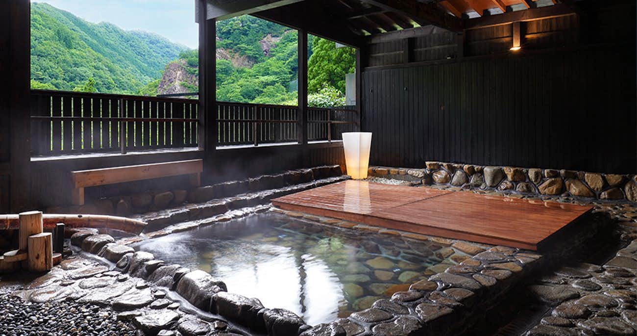 Yubara no Yado Komeya with an open-air stone bath overlooking forested hills.