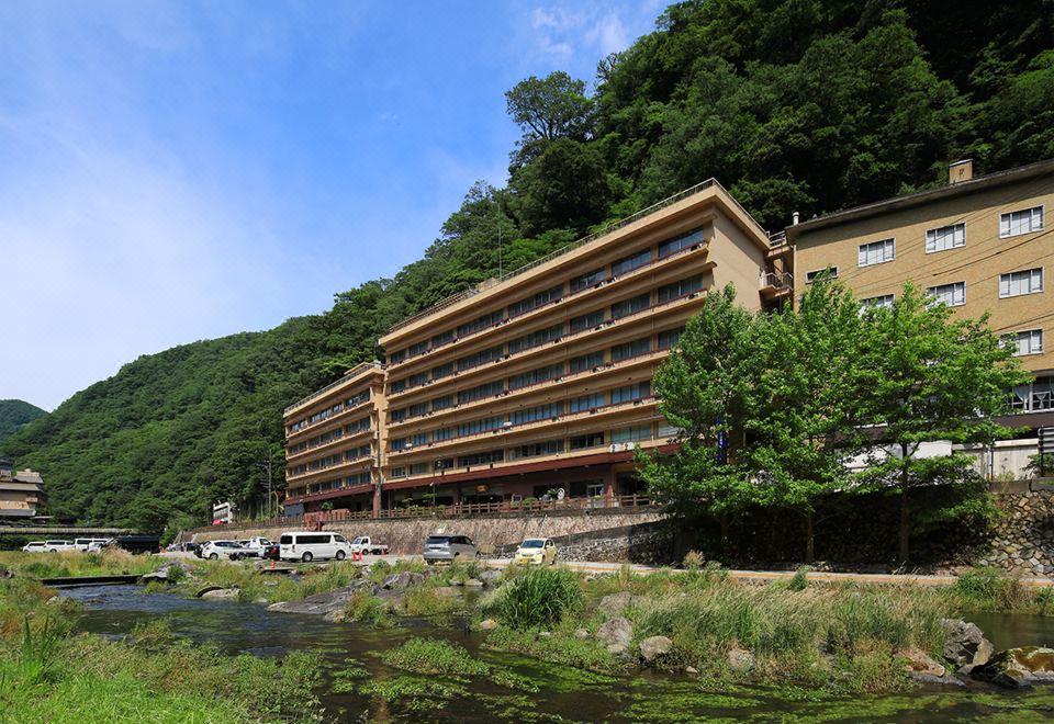 A large hotel beside a river and wooded hills.