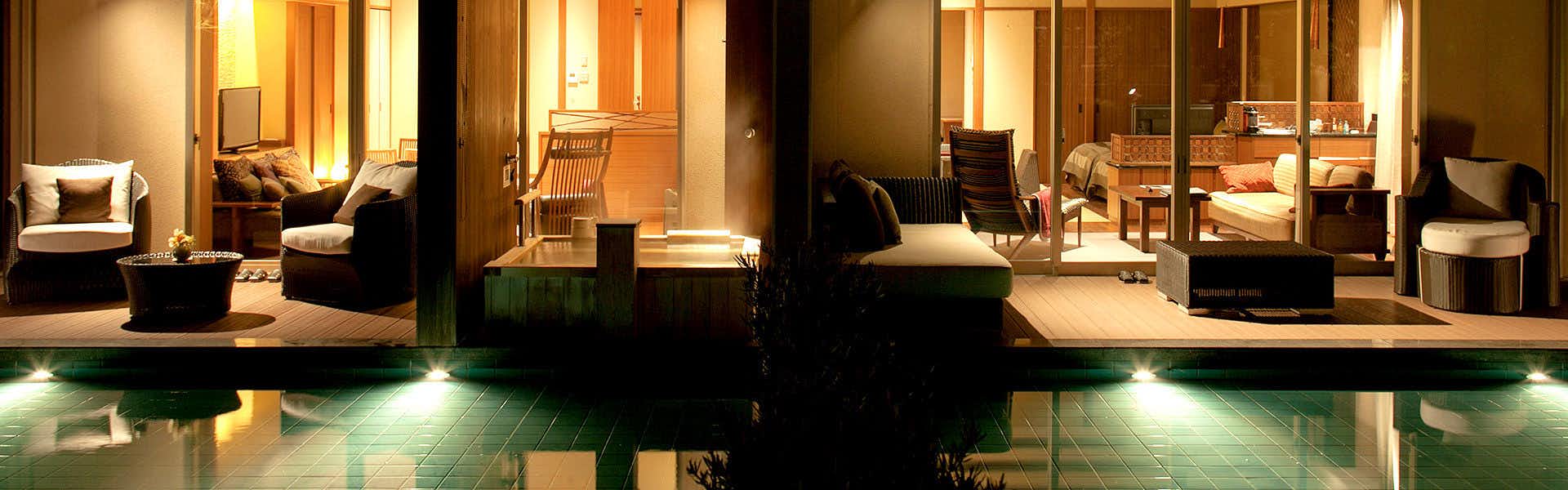 Yamaguchi Yuda Onsen Koki-an Interior passage with tall vertical wooden slat railings, upholstered seating in background, warm ambient lighting, and potted plant in foreground