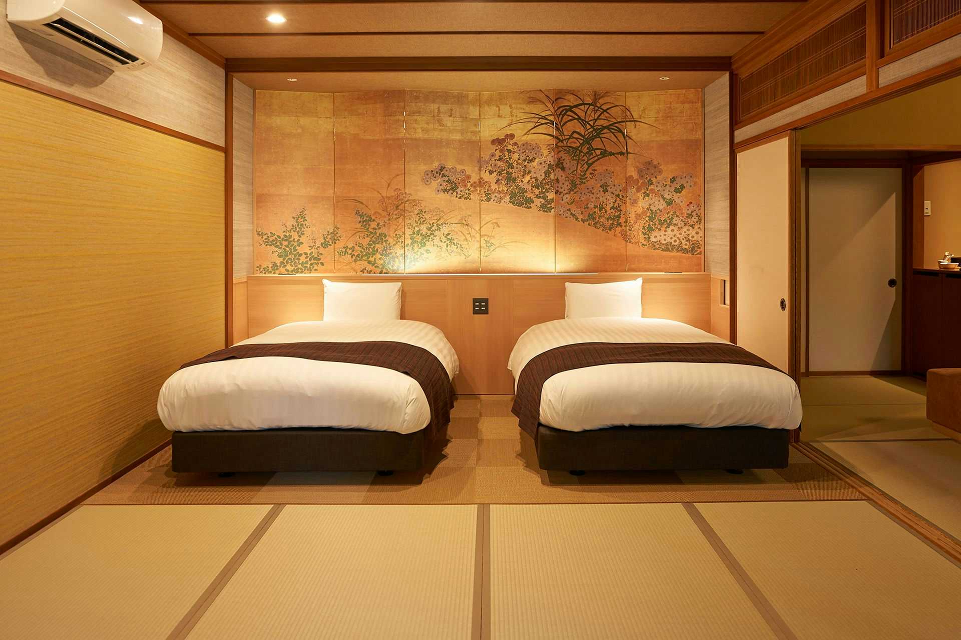 Itoyanagi Bekkan Hanare no Tei Wajoen Bedroom with two single beds on tatami mats, white linens, dark wood frames, golden wood wall panels, framed wall artwork, paper screens, ceiling lights