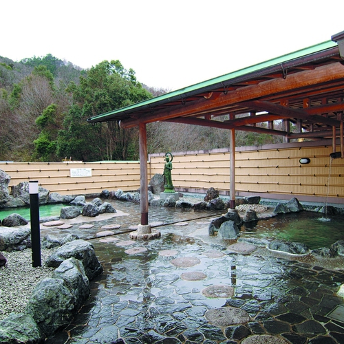 An open-air rock bath beneath a timber roof beside a bamboo fence.