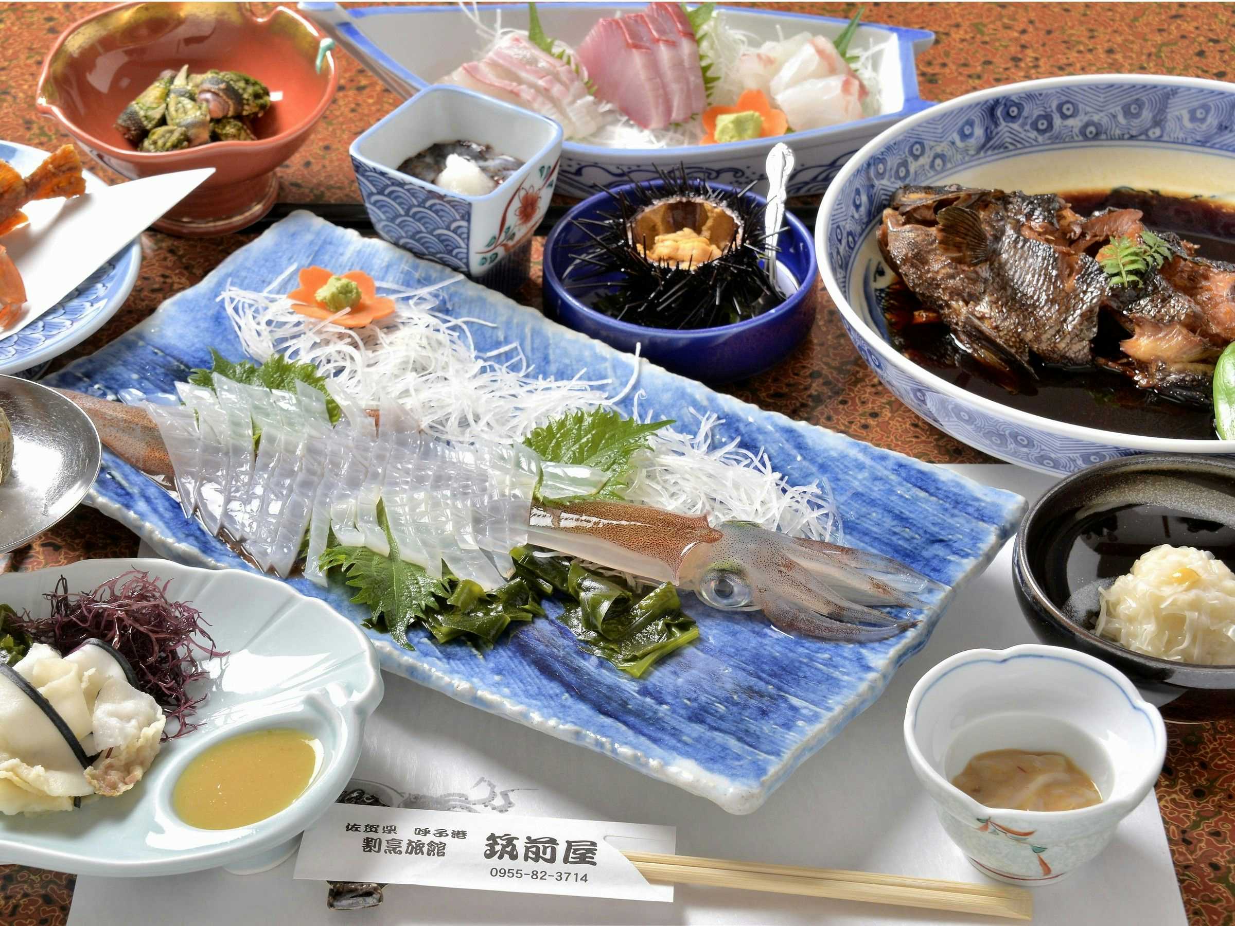Kappo Ryokan Chikuzenya with this scene, where squid sashimi, small dishes and simmered fish fill a dining table.