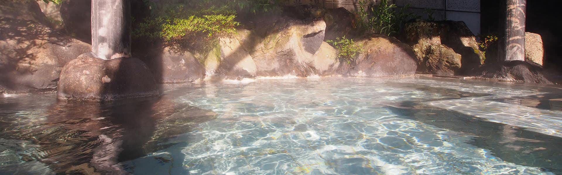Suzunoyado Tofuya Ryokan with an outdoor mineral bath surrounded by rocks and mature trees.