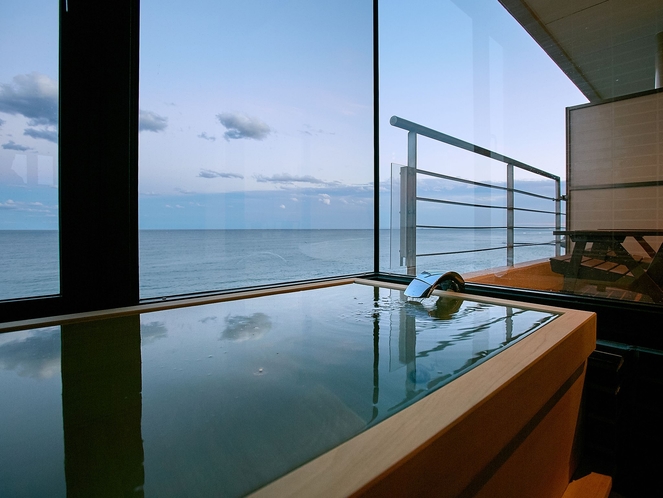 A rectangular bath beside a large window overlooking the sea.
