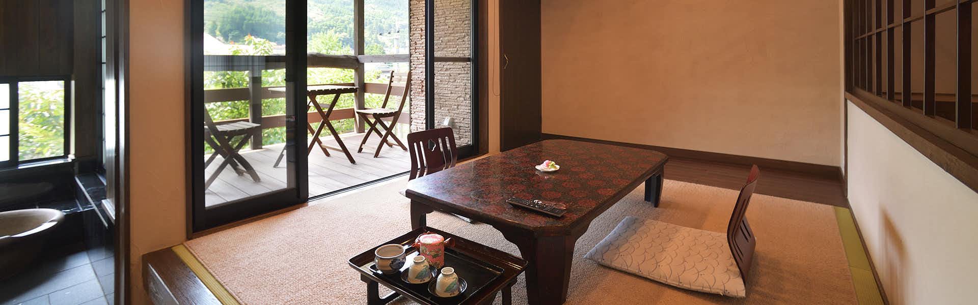 Ryokan Kiyokawa interior space with light flooring, low dark wooden table, ceramic pieces, cushioned seating, window opening to terrace with wooden chairs