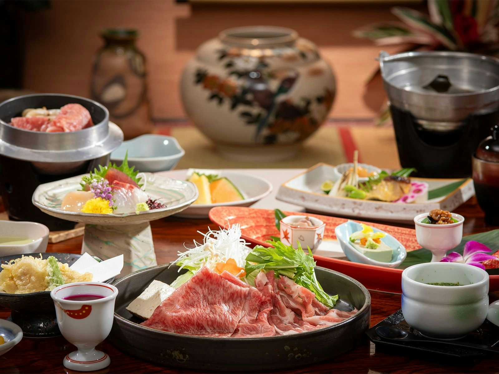 Ichinose with a multi-course dinner arranged around sliced meat and sashimi.