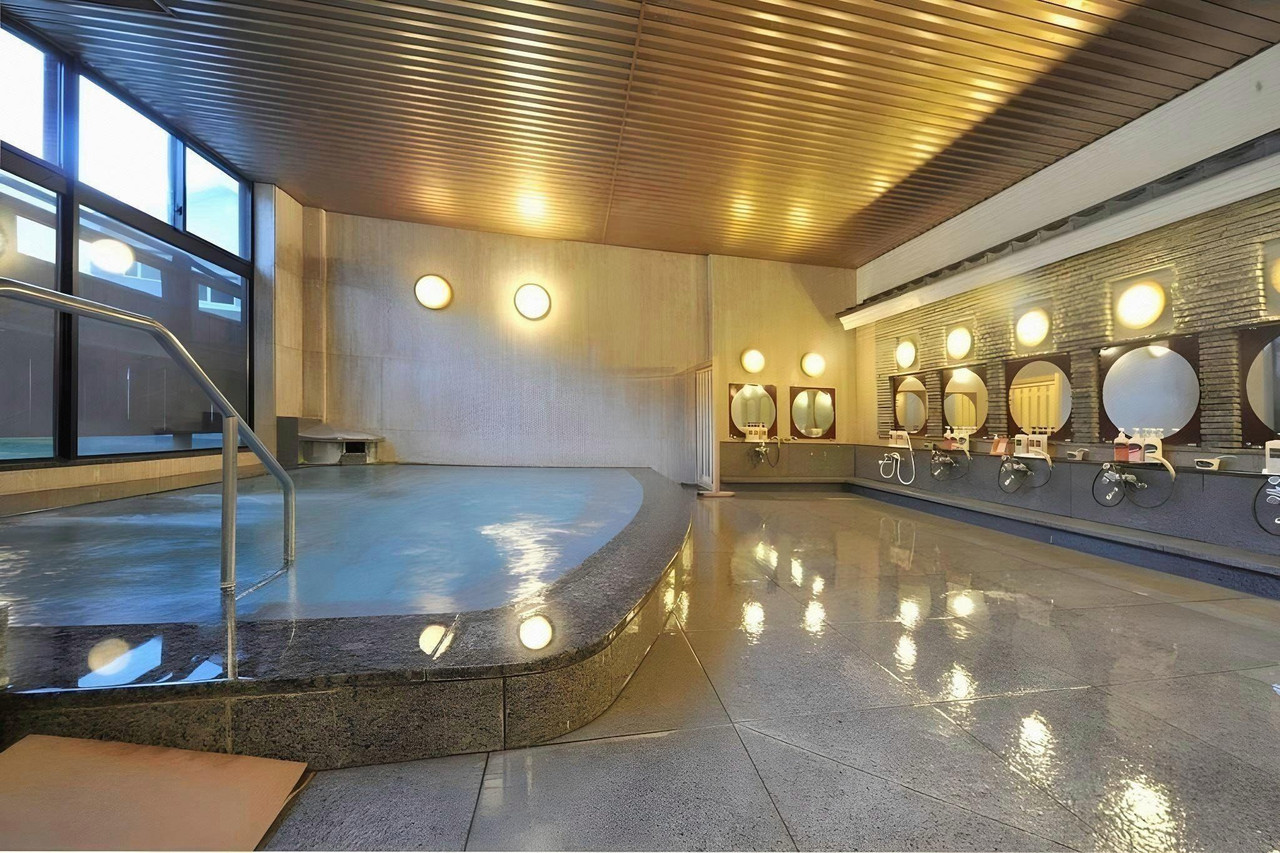 An indoor bath with a rounded edge beside a row of mirrors.