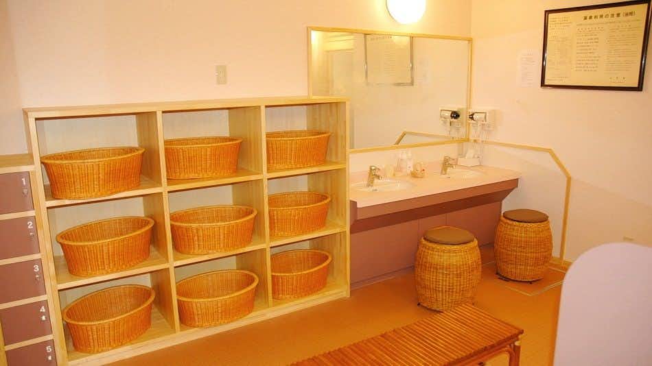 Gassan Shizu Onsen Ryokan Sendai-ya with a bright washroom with wooden baskets, sinks, and tiled floors.