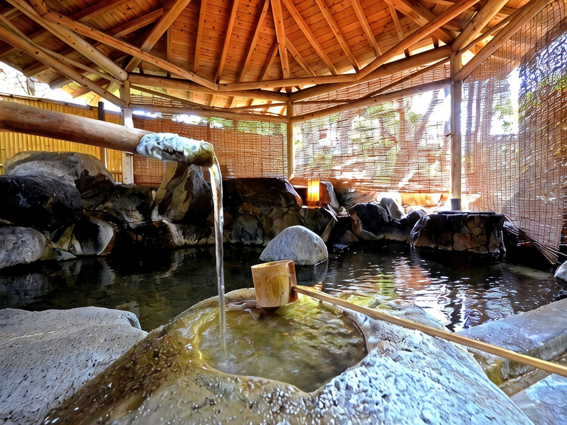 A roofed outdoor bath is surrounded by rocks and greenery.