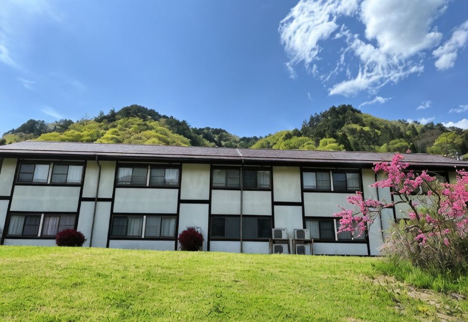 A low building sits beside a landscaped garden and flowering tree.