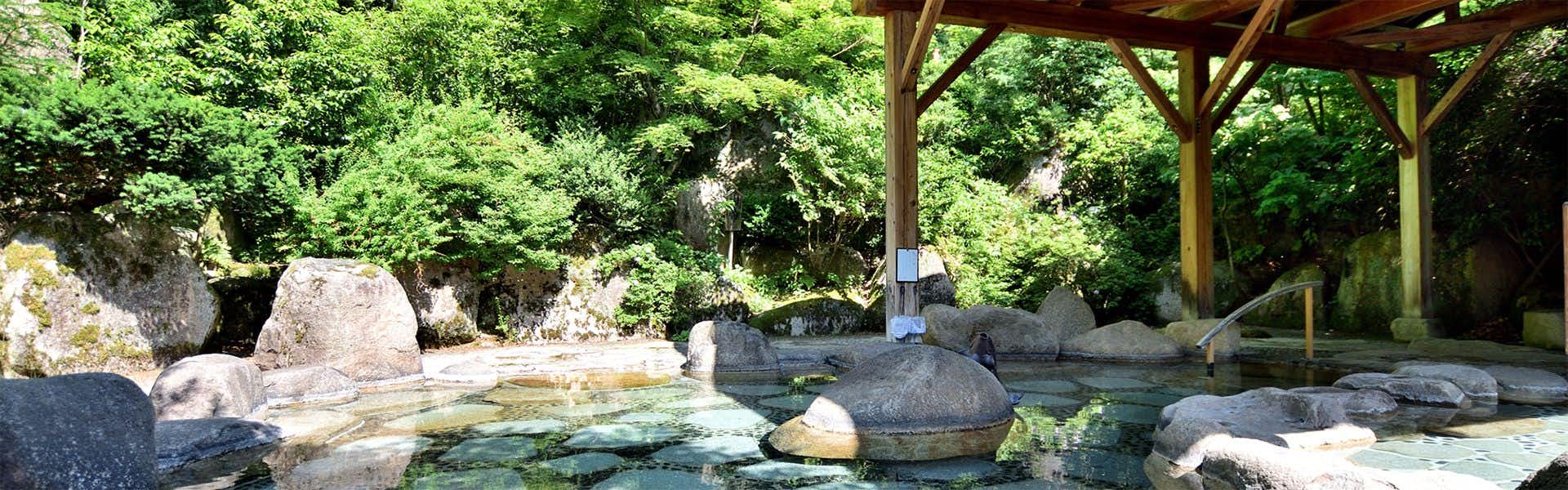 Chouseikan Stone boulders in water, green forest foliage canopy, wooden beam structure visible