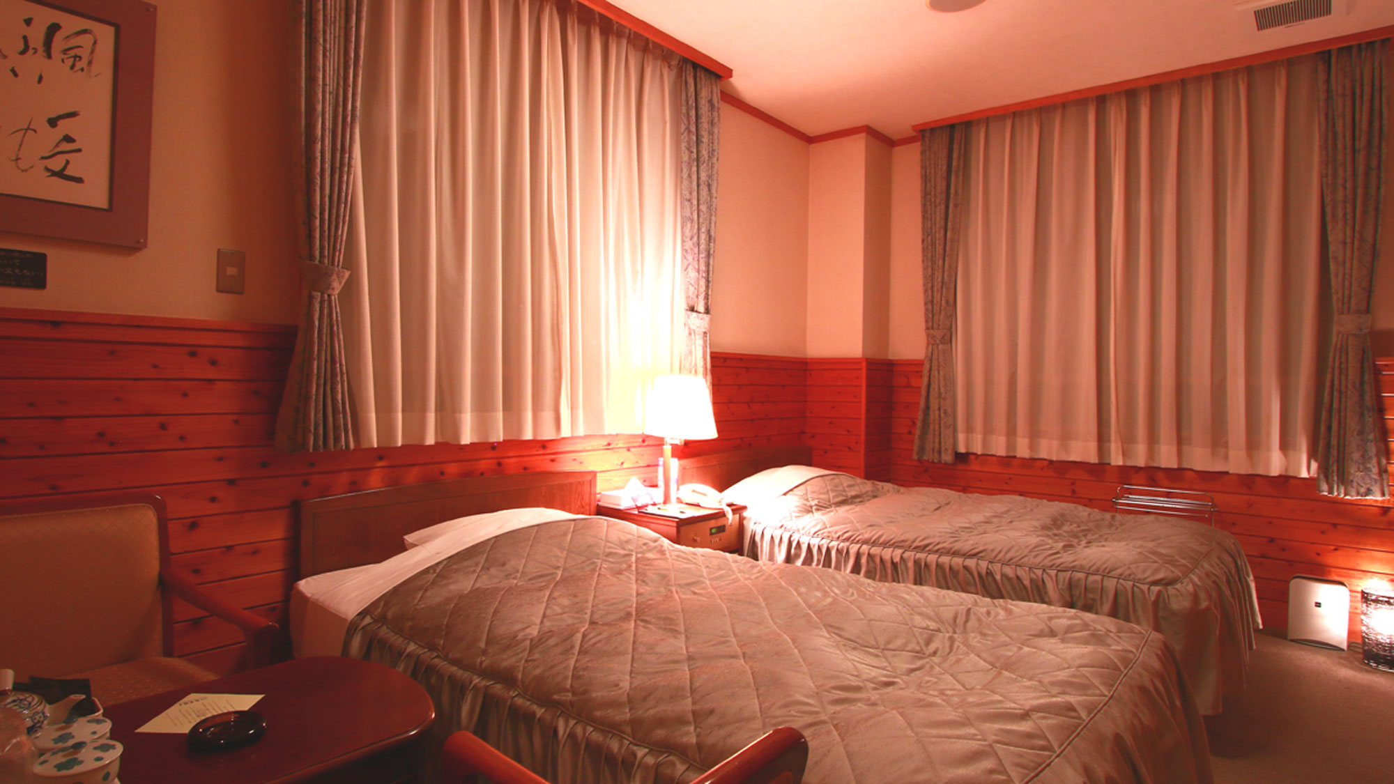 A warmly lit twin bedroom with curtains and wooden wall panels.