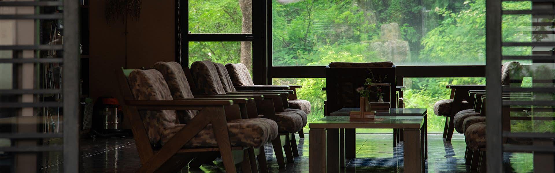 Oshimizu no Yu Tsutaya Interior lounge with brown seating furniture, dark wood elements, and expansive windows showing green landscape