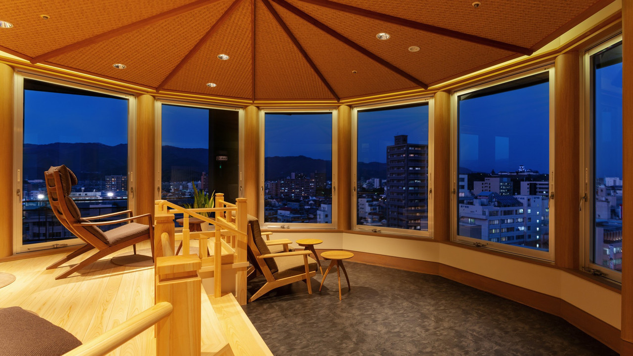 A corner seating area looks across the city from tall windows.