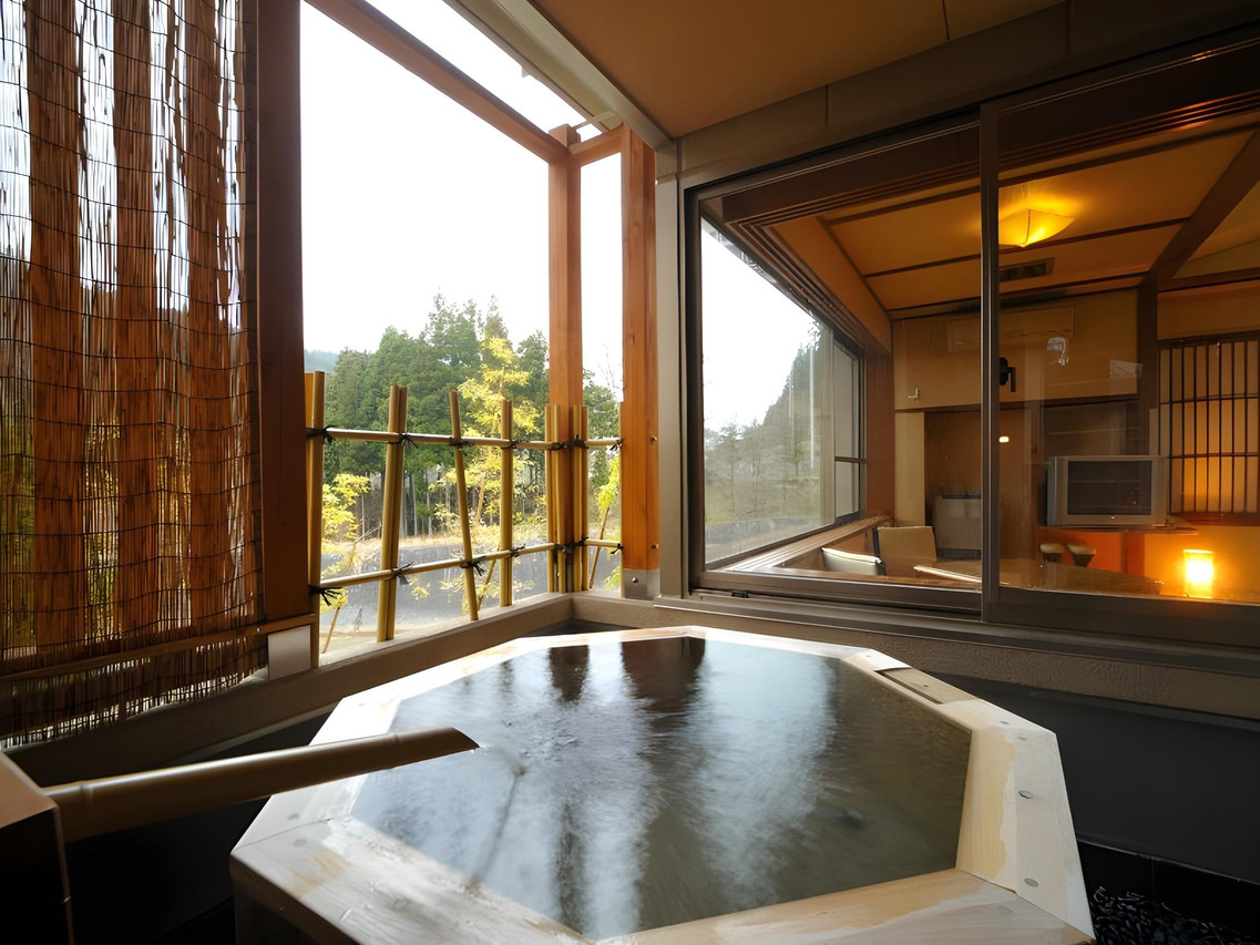 An angular bath beside wooden screens and a guest room window.