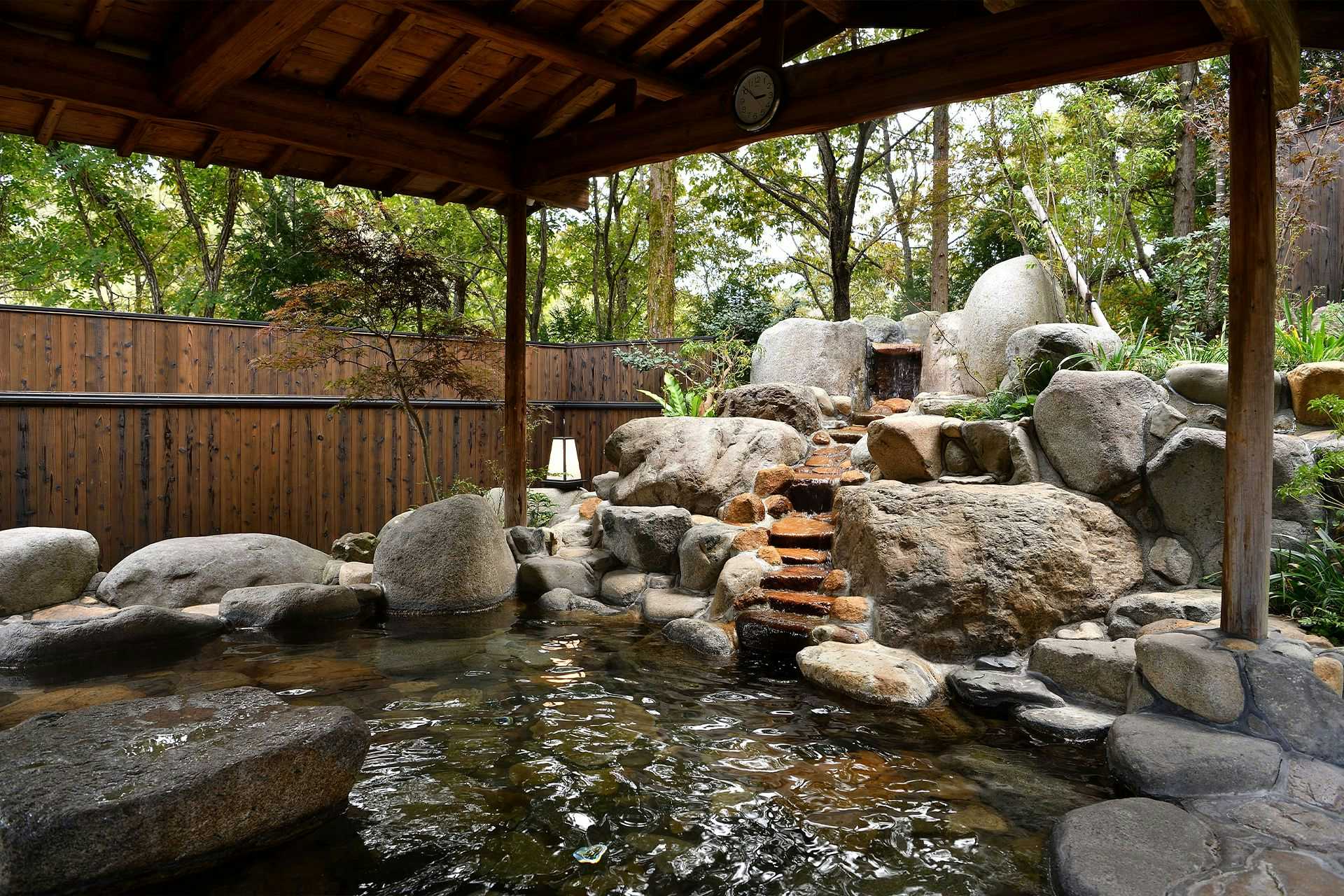 Yunogo Onsen Yunogo Bishunkan with an open-air rock bath shaded by dense woodland.