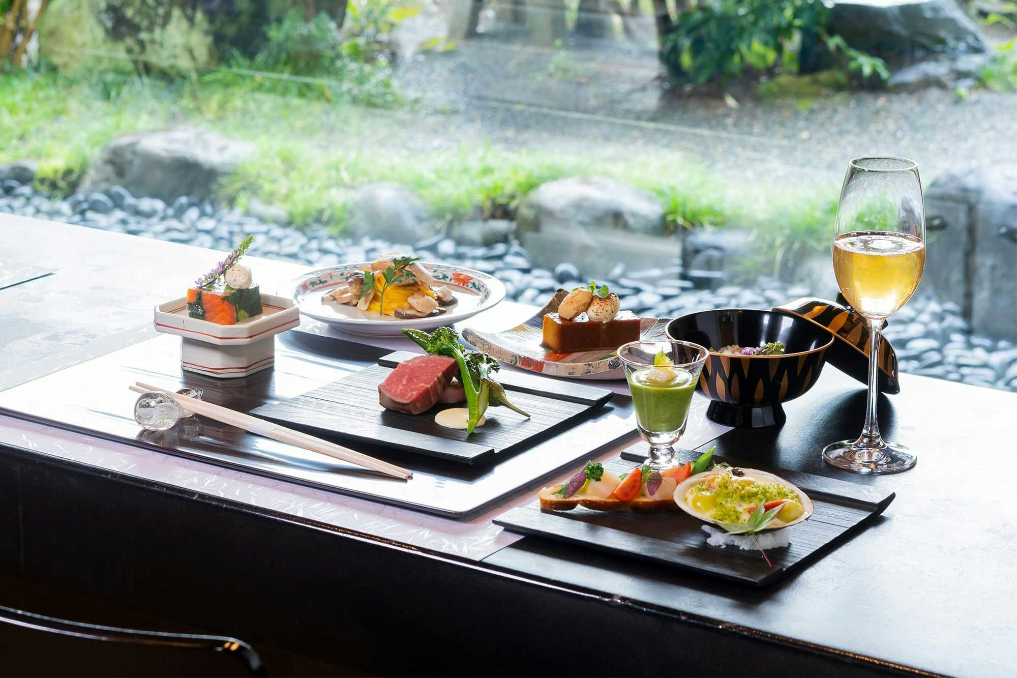 Kappo Ryokan Shinkanou with a Japanese dinner arranged beside broad windows overlooking garden greenery.