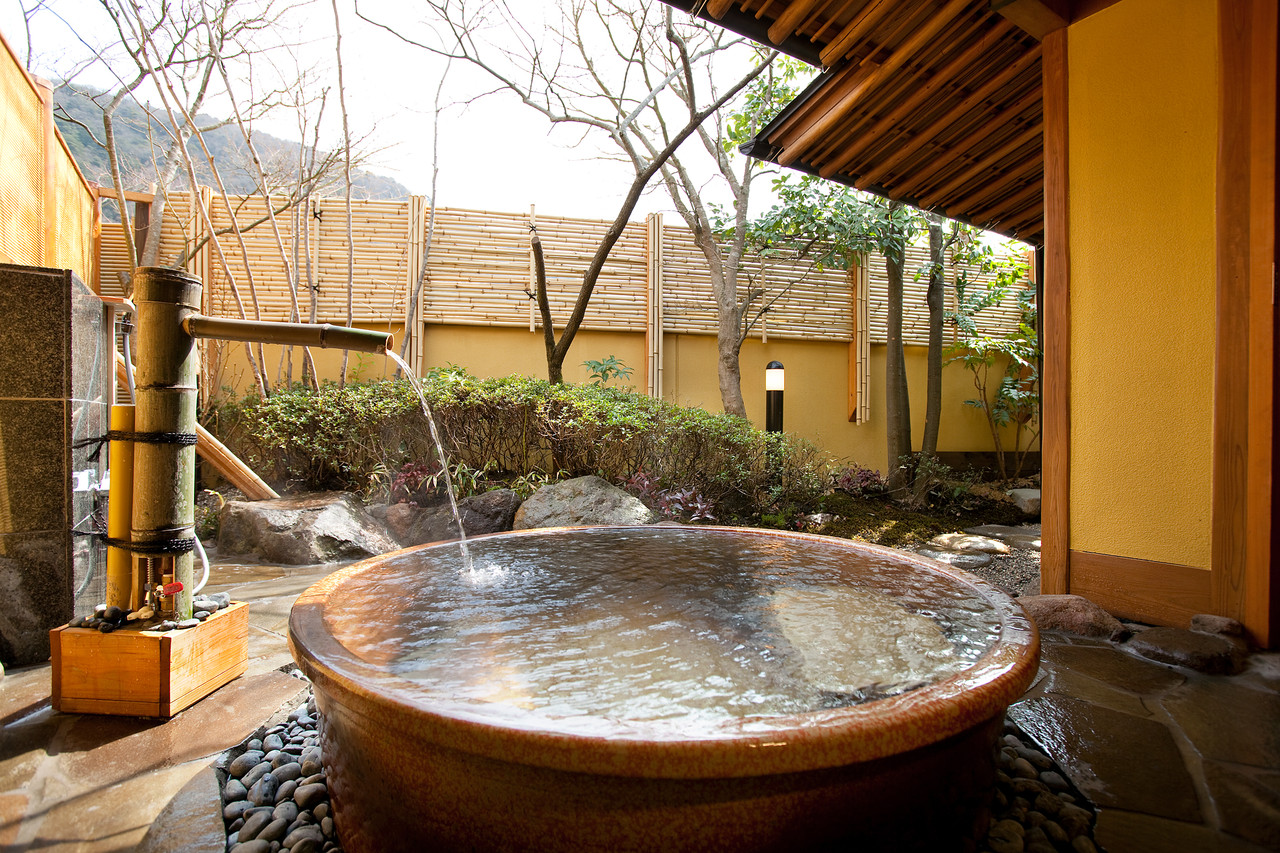 A round outdoor tub beneath a roof beside bamboo fencing.
