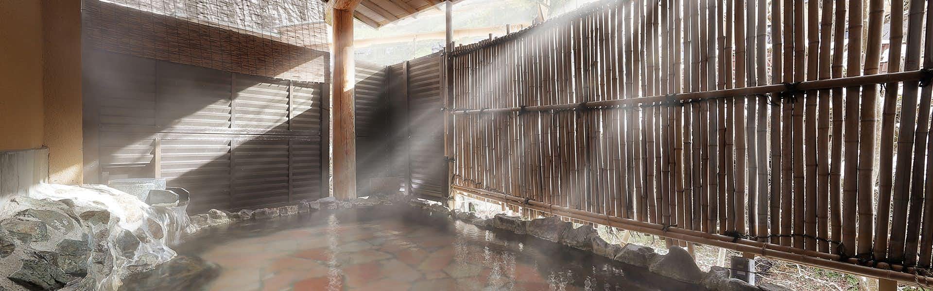 Yamayuri Inn with a steaming open-air rock bath enclosed by bamboo screens.