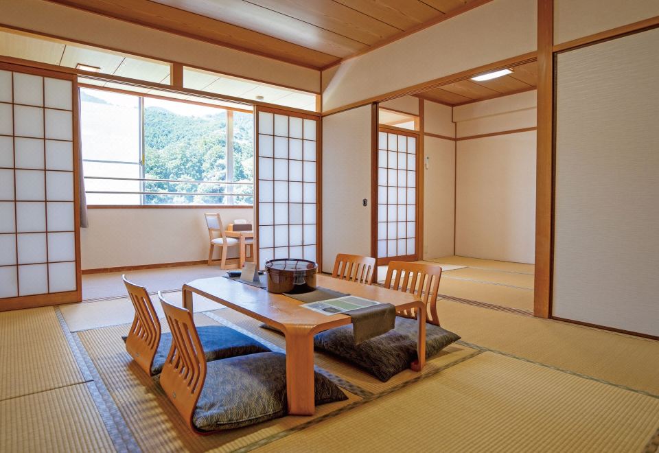 A Japanese guest room with a low wooden table, cushions, and garden-facing windows.