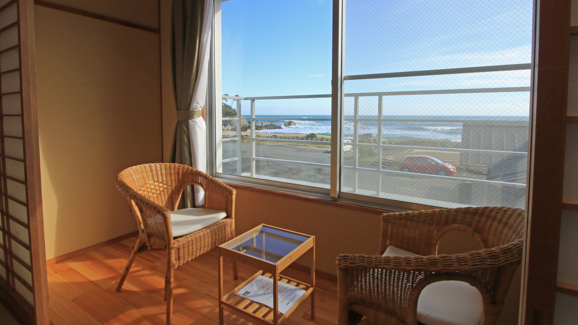 Wicker chairs beside large windows overlooking the sea.