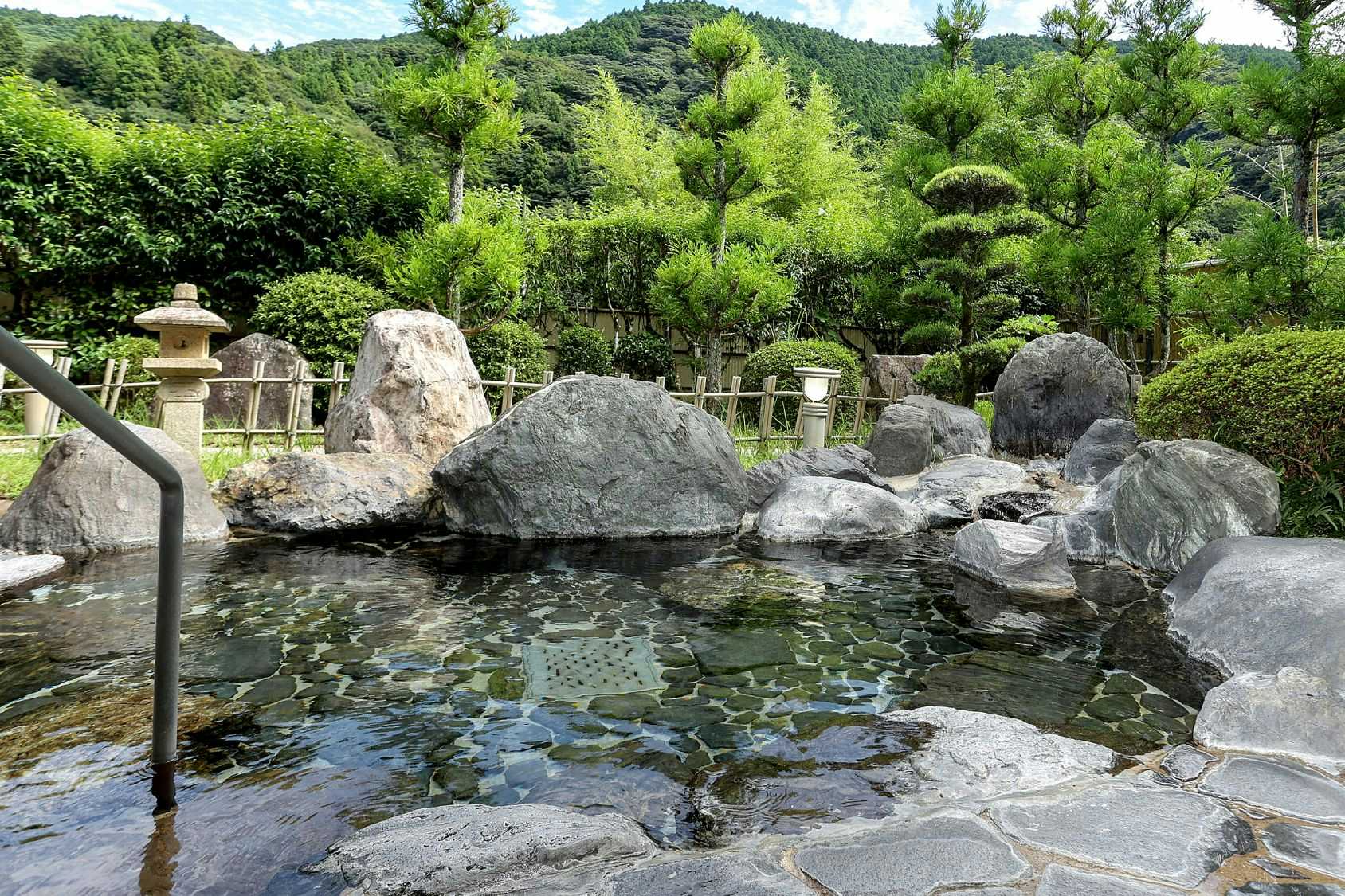 Ichinomata Onsen Kanko Hotel with an outdoor rock bath surrounded by clipped garden shrubs.