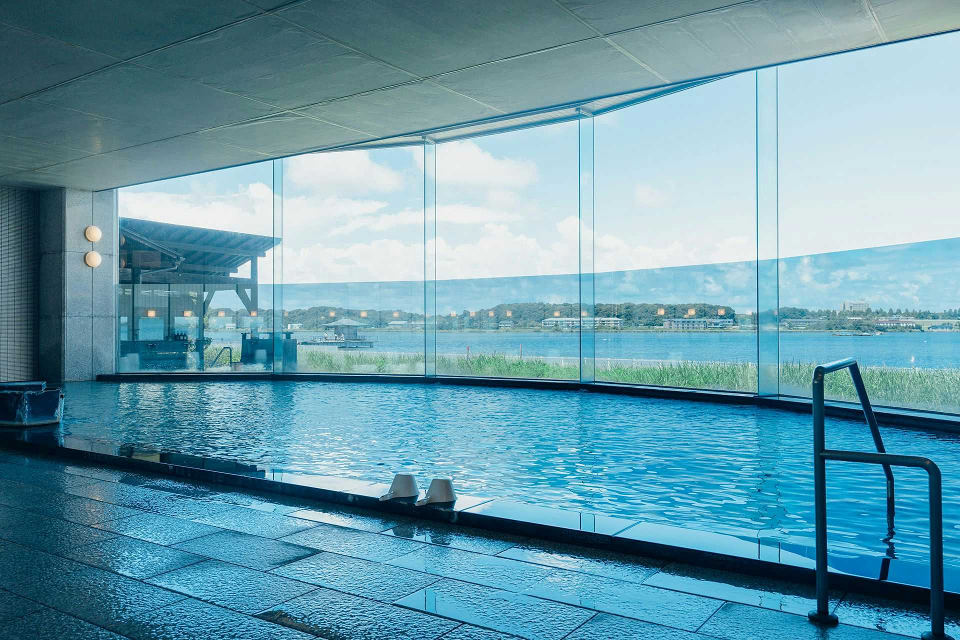 Lakeside Inn Morimoto Large indoor bath with tiled deck, metal handrail, bathing stools, and floor-to-ceiling windows overlooking water
