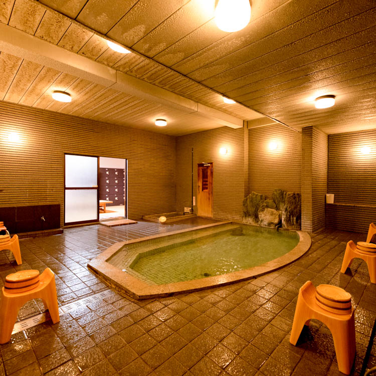A warm indoor bath is surrounded by dark tile and washing stations.