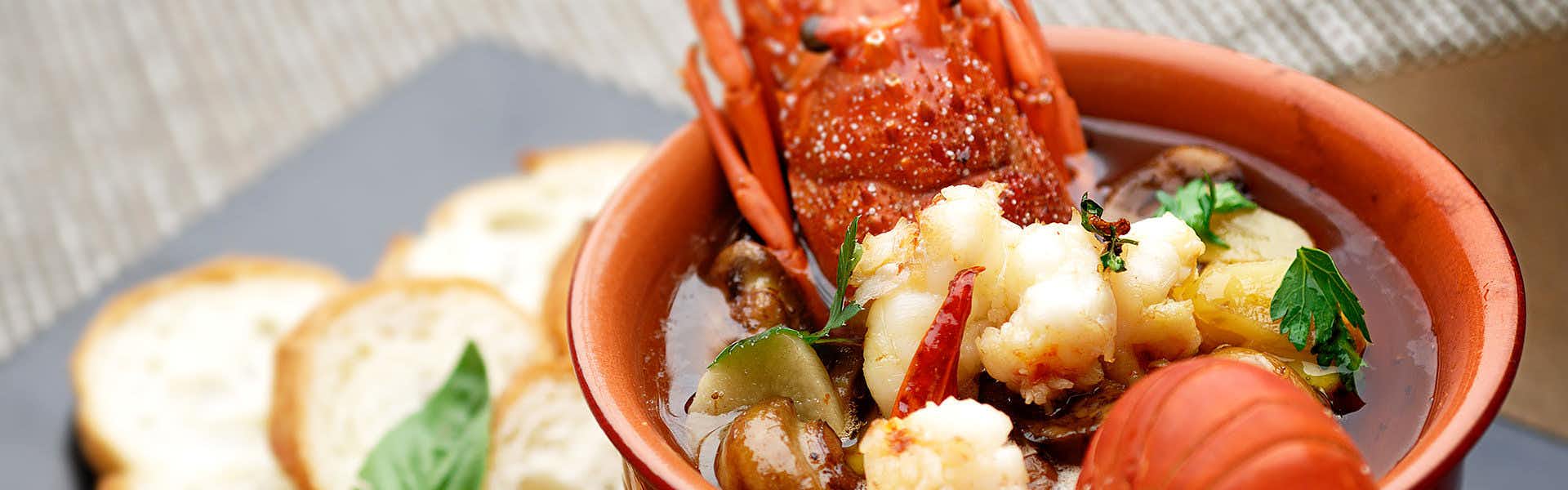 Kouyurou Ikawa with lobster and vegetables presented in a red ceramic bowl.