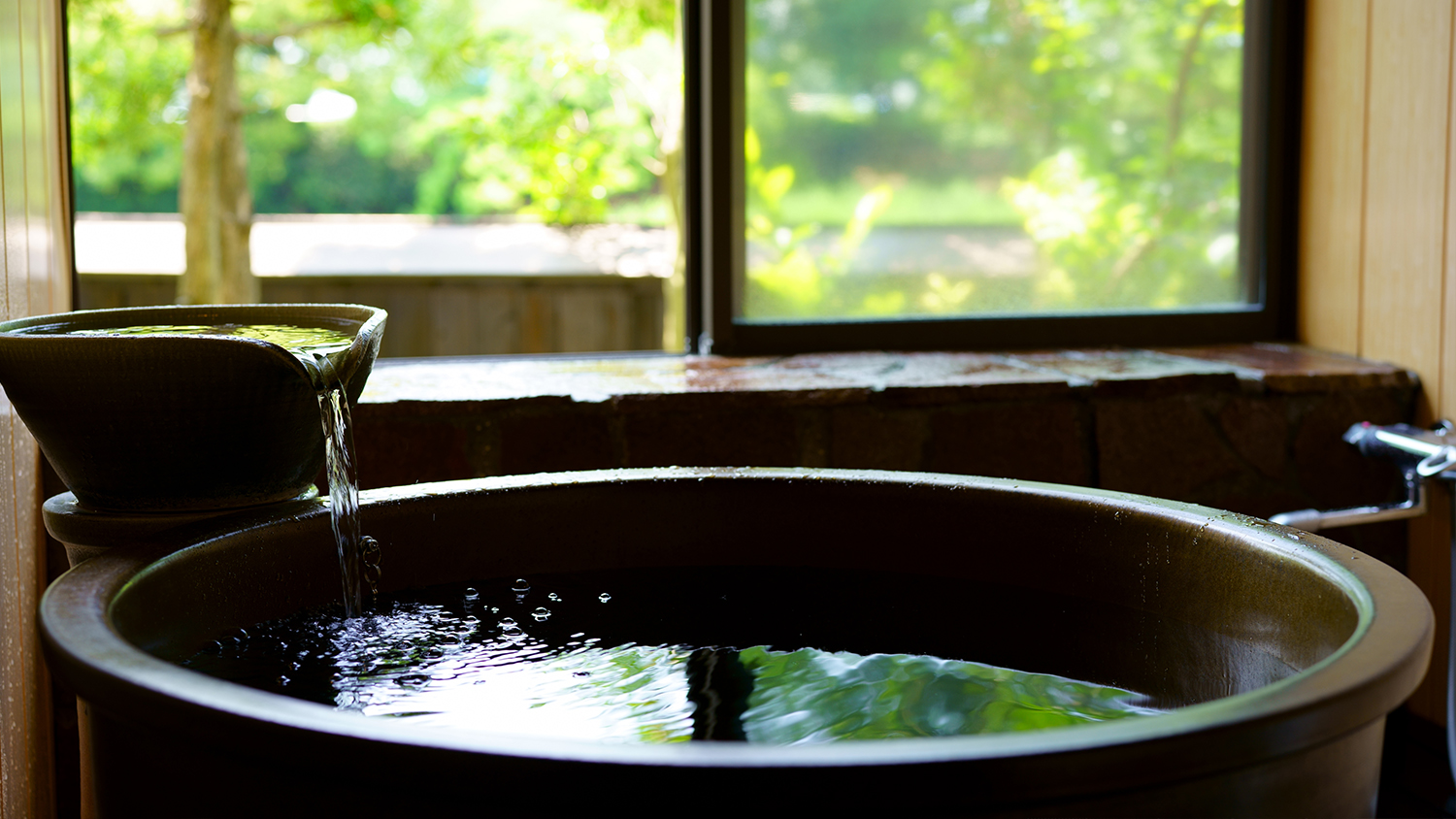 A round tub is positioned beside a window overlooking greenery.
