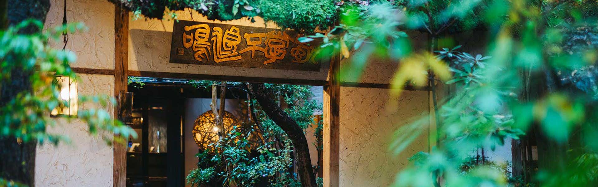 Kurokawa-so with a timber entrance sign framed by leafy branches.