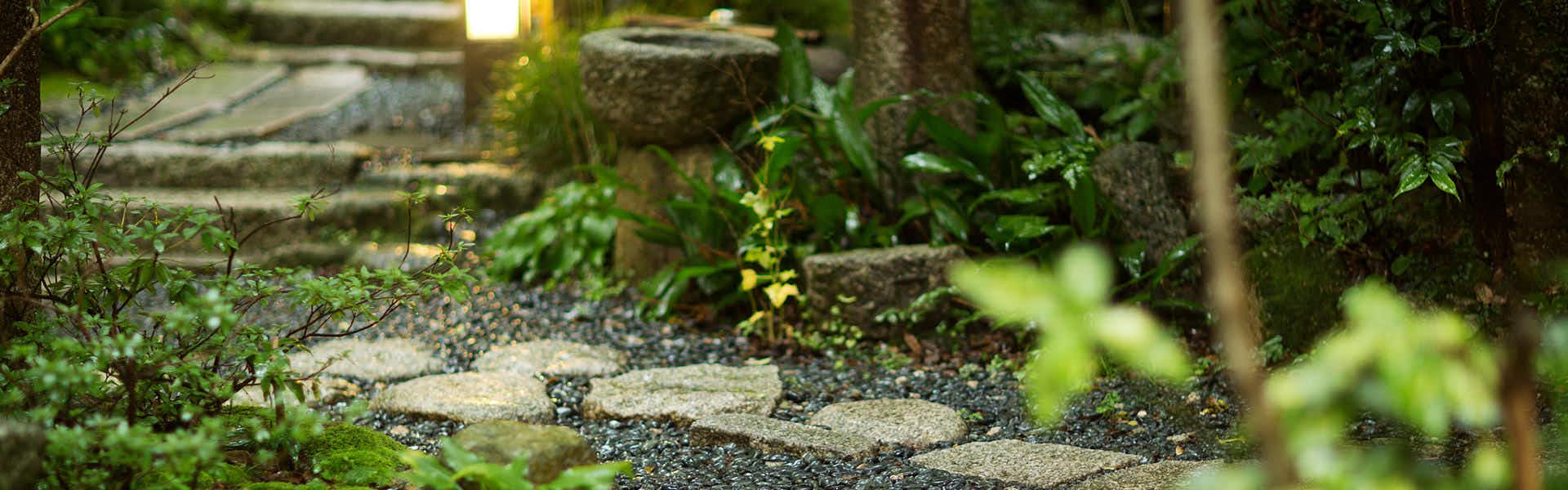 Ryokan Kotobukitei garden pathway with tan stepping stones on gravel bed surrounded by dense green foliage and layered vegetation.
