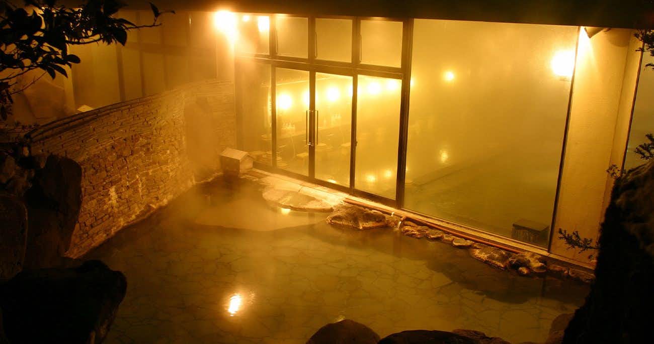Fujiya Hotel Outdoor bath basin with warm golden lighting at night, stone walls, and surrounding dark area.