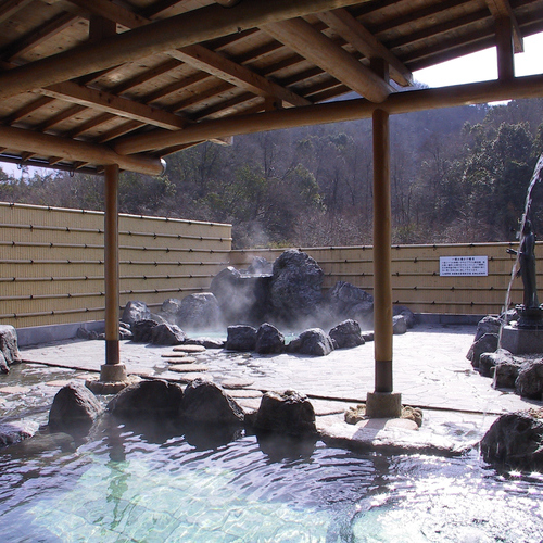 A roofed outdoor rock bath with steam rising from the water.