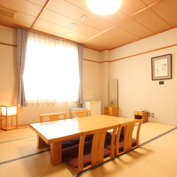 A Japanese guest room with a low table, floor chairs, and a large curtained window.