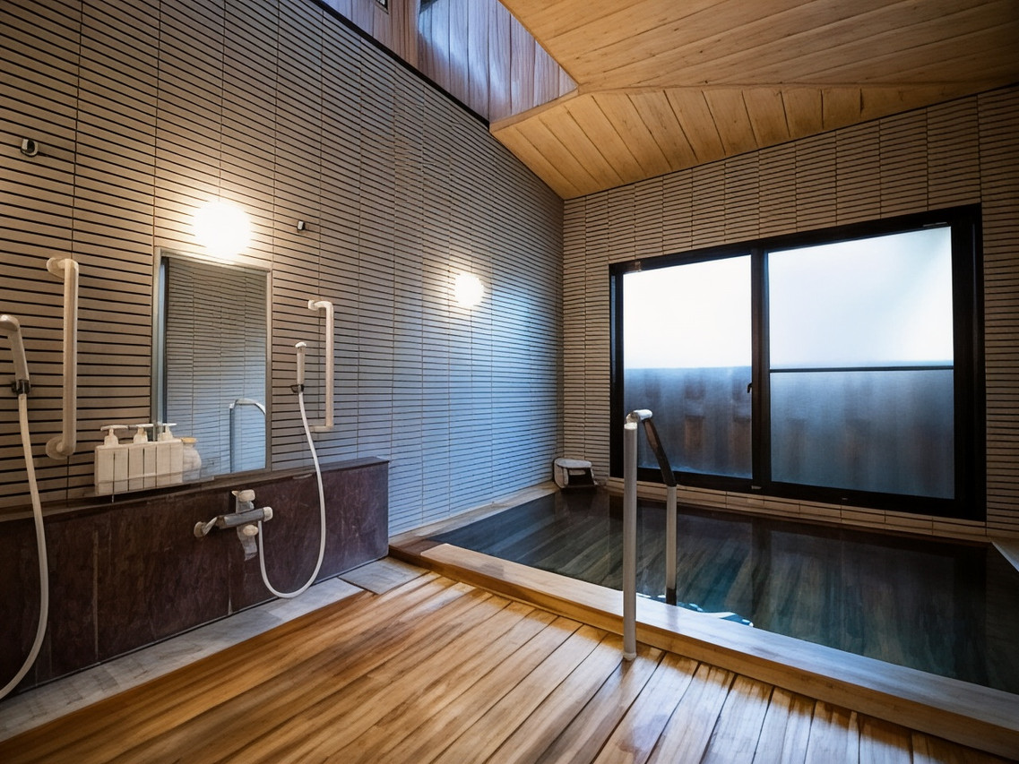 A dark tiled bathing room with a shower area.