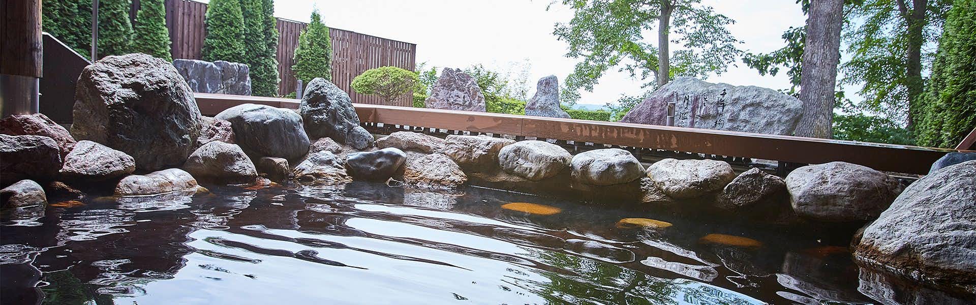 Kangetsuen with an outdoor rock bath surrounded by mature trees.