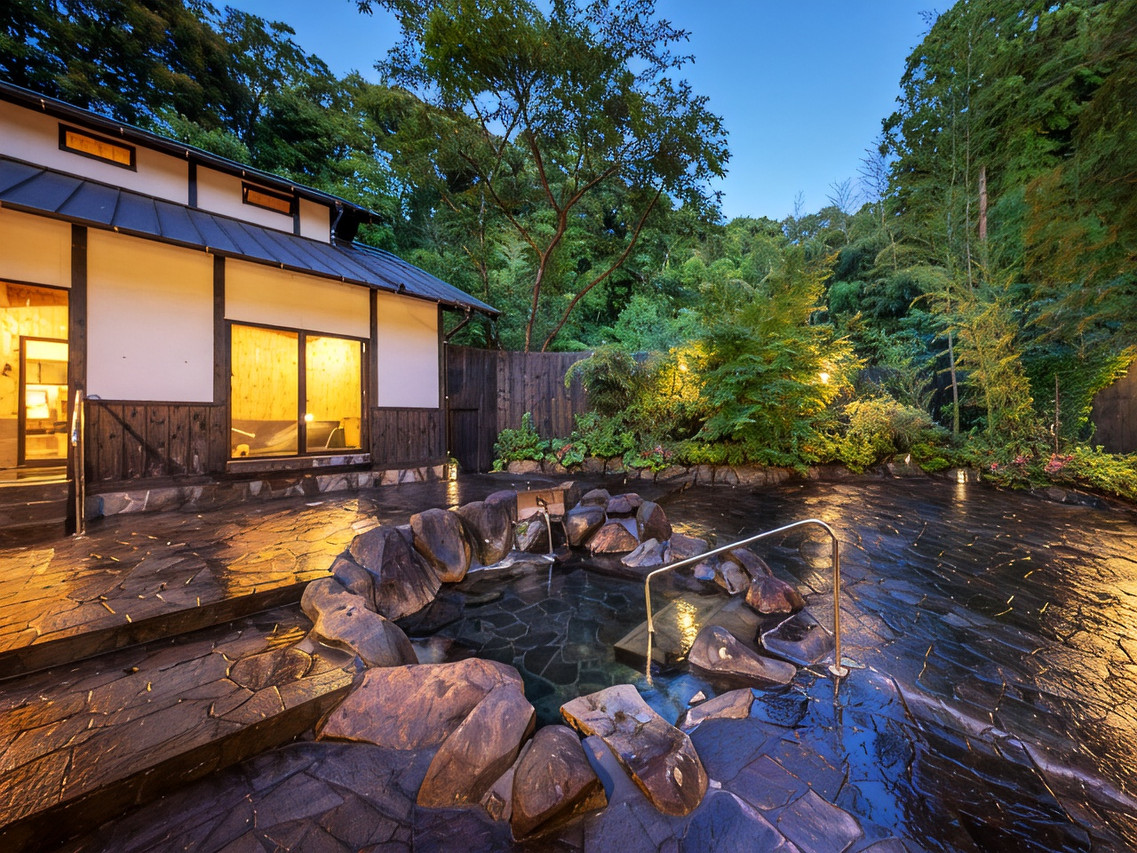 A traditional wooden bathhouse sits beside a rocky garden stream.