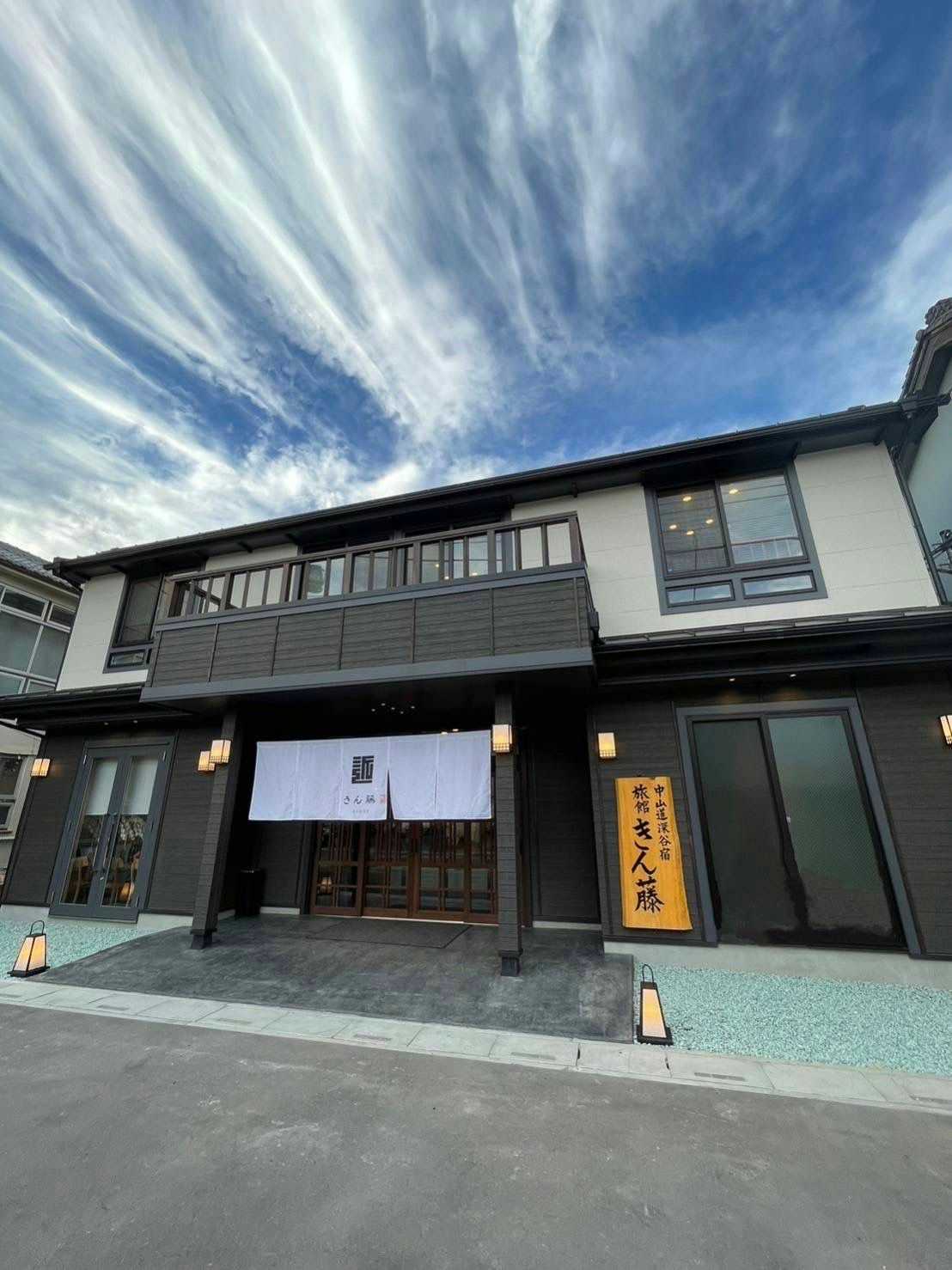 Ryokan Kintou with the dark timber street facade beneath streaked white clouds.