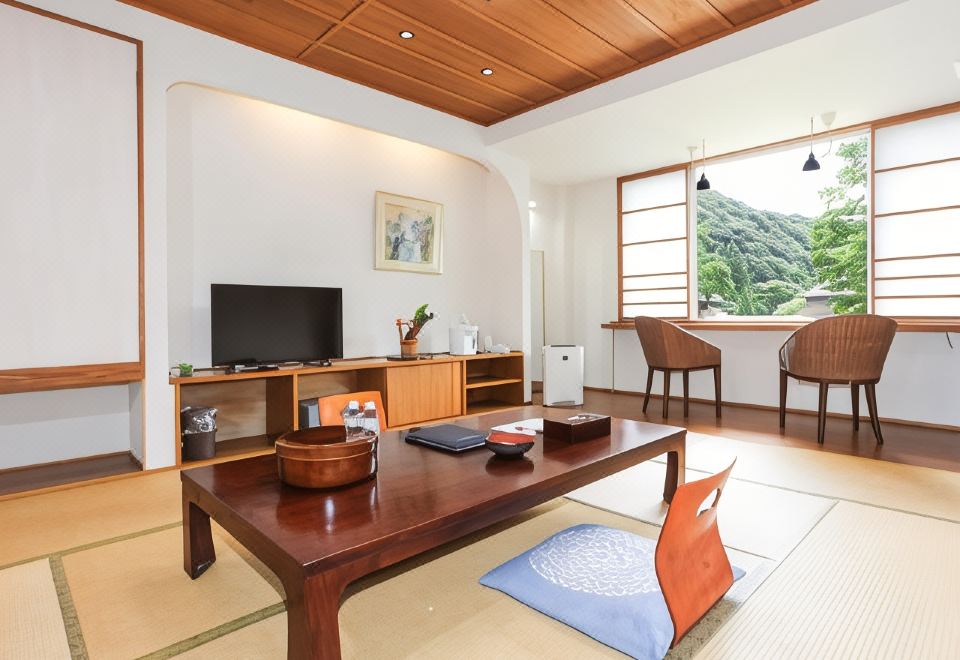 A bright tatami guest room with a low table, television, and window-side chairs.