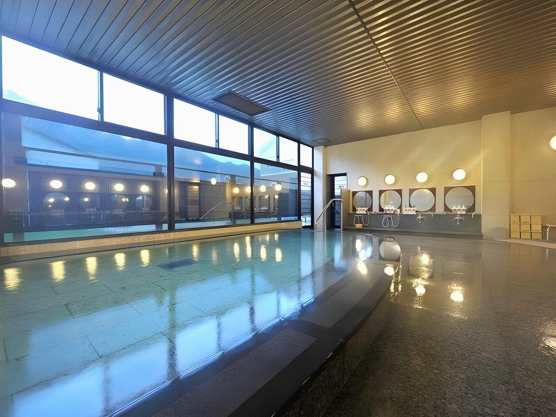A long indoor bath beside large windows overlooking the evening sky.
