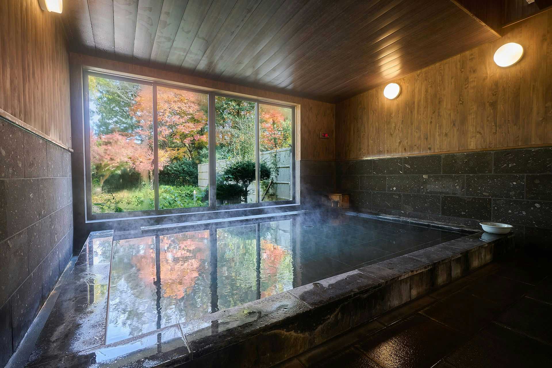 Minami Aso Tawarayama Onsen Ryokan Chikurakutei Bath with wooden walls and ceiling, large windows with outdoor view, water surface with reflections
