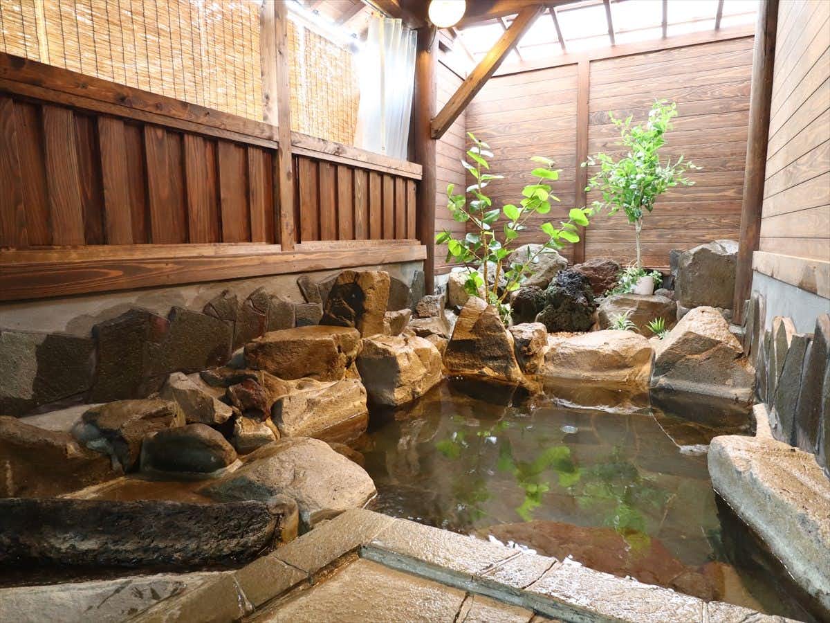 Shukuro Banya with an open-air rock bath beneath bamboo screens and timber beams.