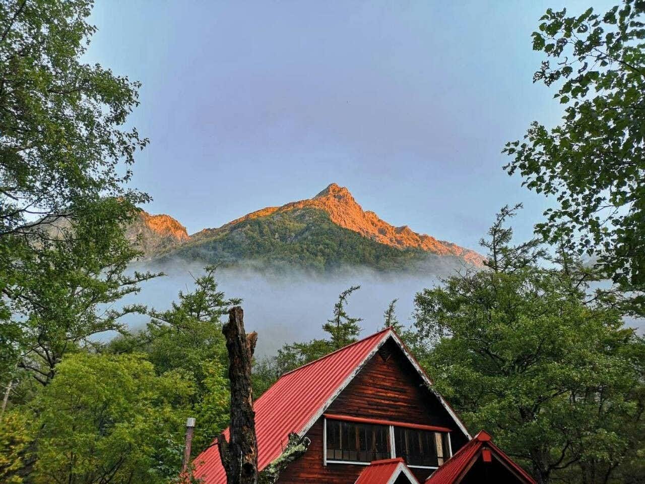 Kamikochi Yama no Hidaya with a red-roofed lodge framed by forest and mountain slopes.