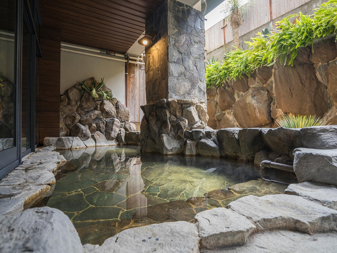 A rock-lined outdoor bath beside a window.