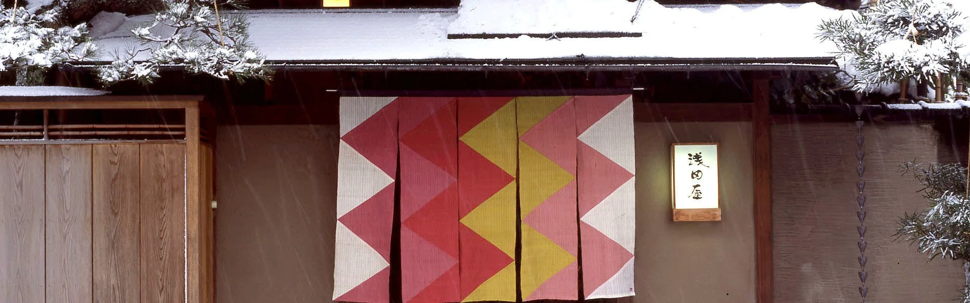 Asadaya's winter entrance in Kanazawa with geometric red and gold noren under snow
