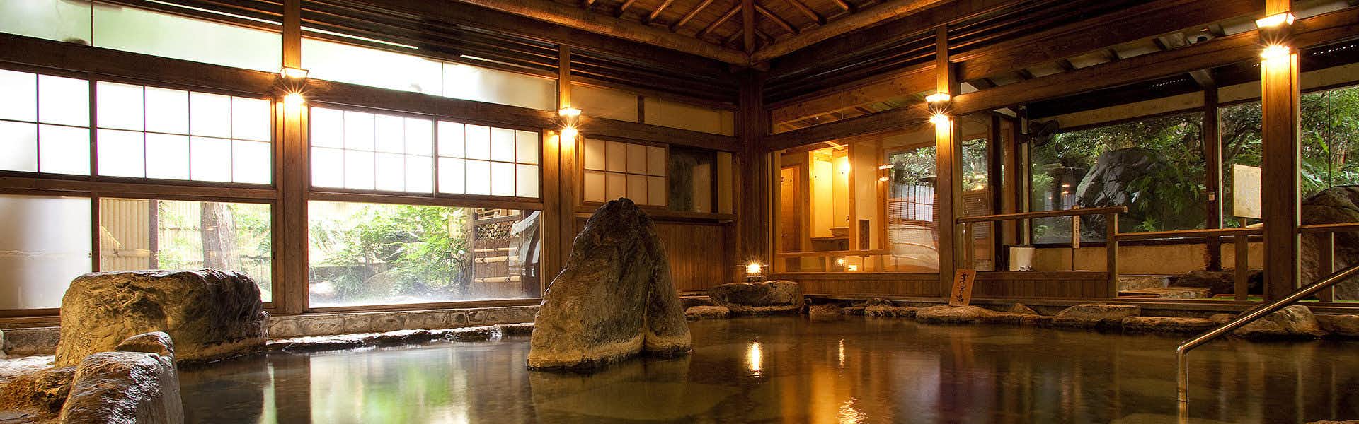 Izanro Iwasaki with an indoor stone bath framed by shoji windows and timber beams.