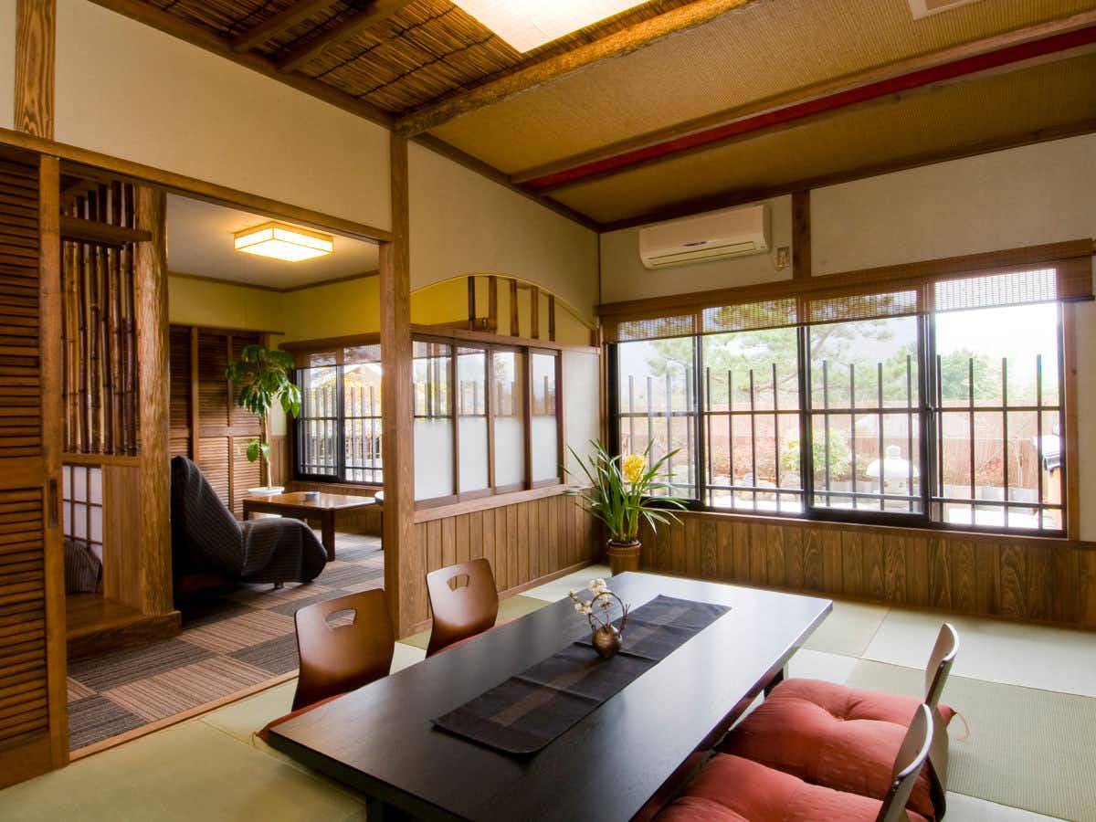 Kaede no Shoja Large central table with dark top, red cushioned chairs, wooden ceiling beams, multi-paned windows, indoor potted plant.