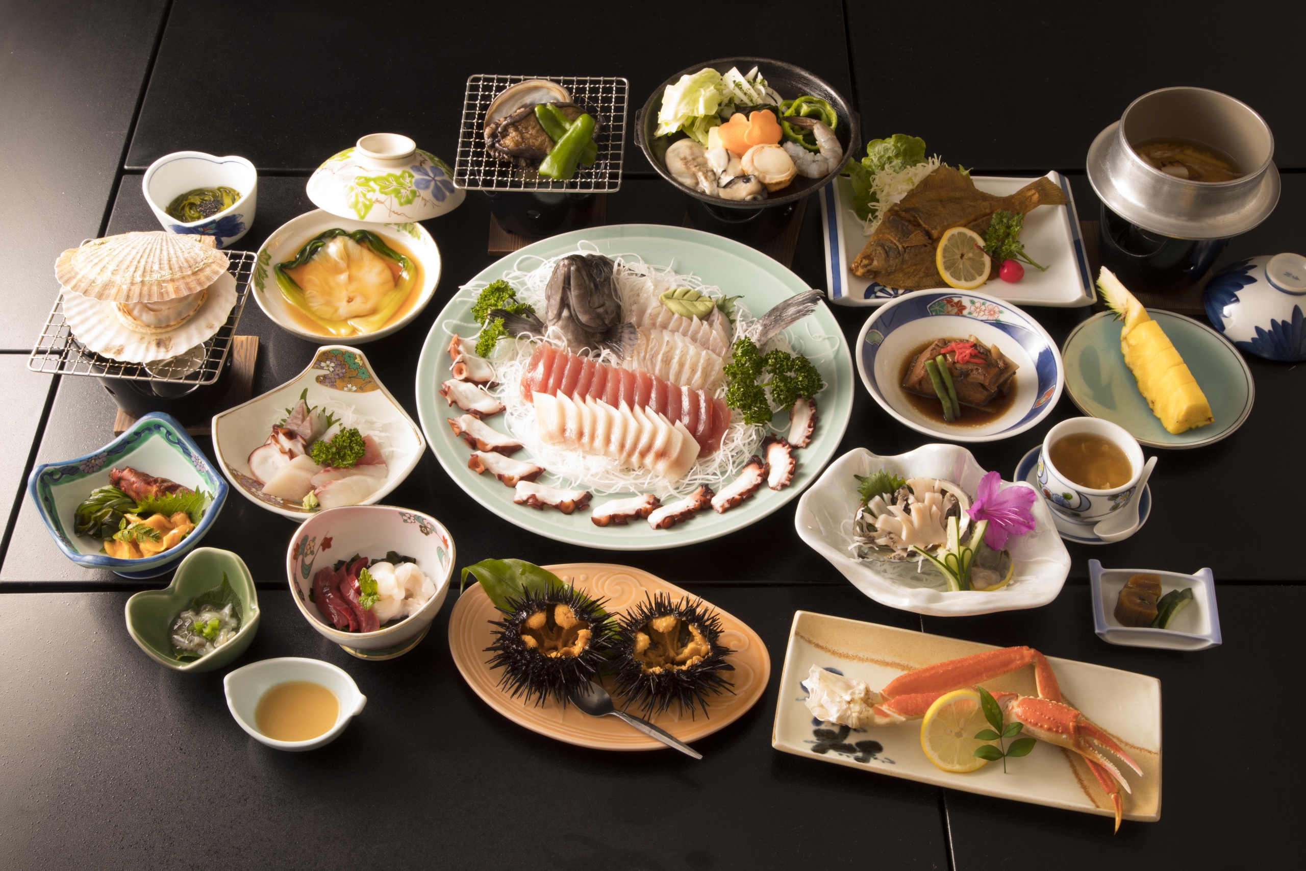 Sashimi, shellfish, grilled fish, tempura, rice, soup, and small dishes fill a dining table.