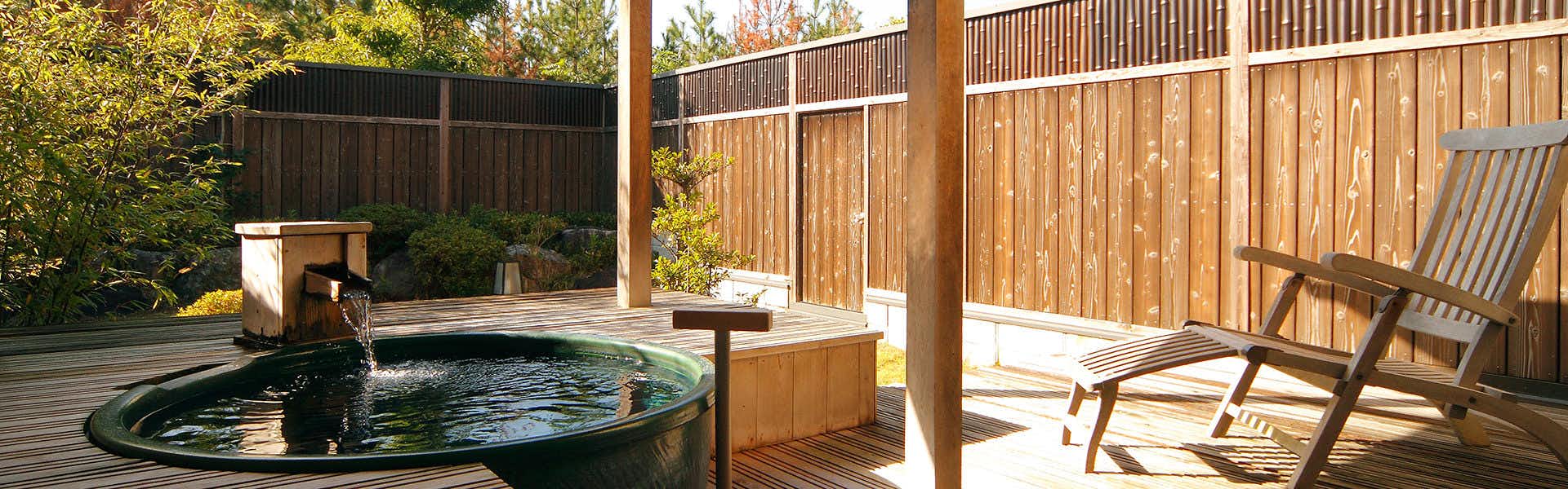 Kappo Ryokan Echizen Mangetsu Round blue outdoor bathing basin set into wooden deck enclosed by tall wood fencing.